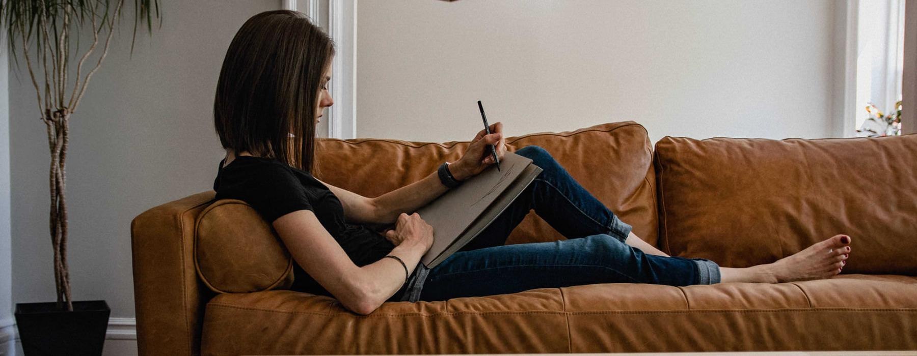 woman lies on a couch and draws on a large sketch pad